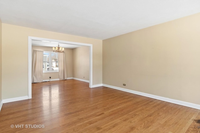 empty room with an inviting chandelier, baseboards, and wood finished floors