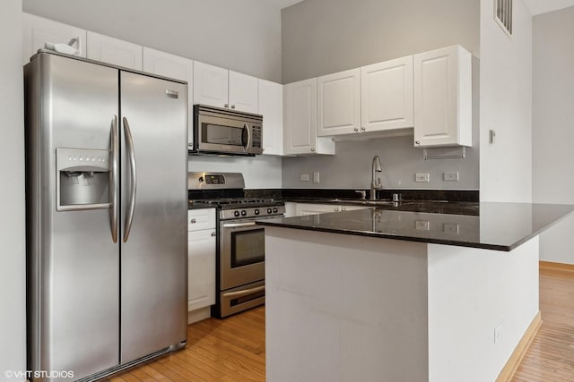 kitchen with stainless steel appliances, light hardwood / wood-style floors, sink, dark stone counters, and white cabinets