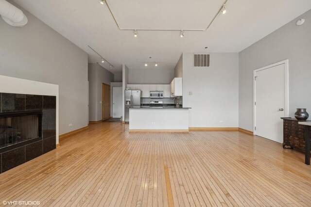 unfurnished living room with a tile fireplace, track lighting, and light hardwood / wood-style floors