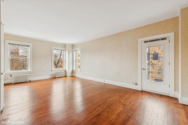 empty room featuring light wood-type flooring, radiator heating unit, and a wealth of natural light