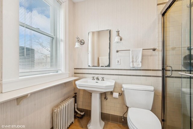 bathroom with a shower with shower door, toilet, radiator heating unit, and sink