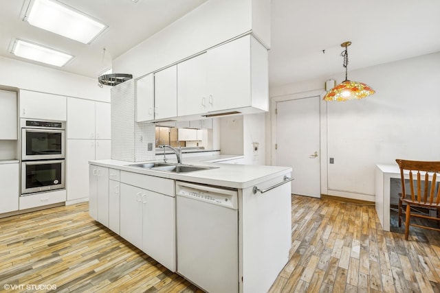 kitchen with white dishwasher, sink, stainless steel double oven, decorative light fixtures, and white cabinetry