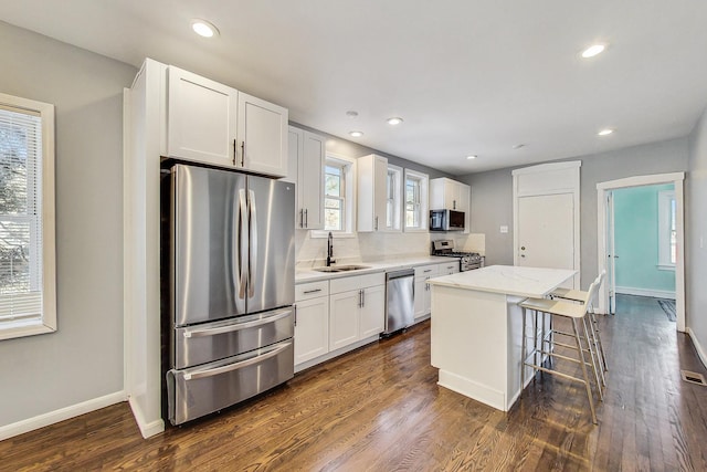 kitchen featuring appliances with stainless steel finishes, a kitchen bar, sink, a center island, and white cabinetry