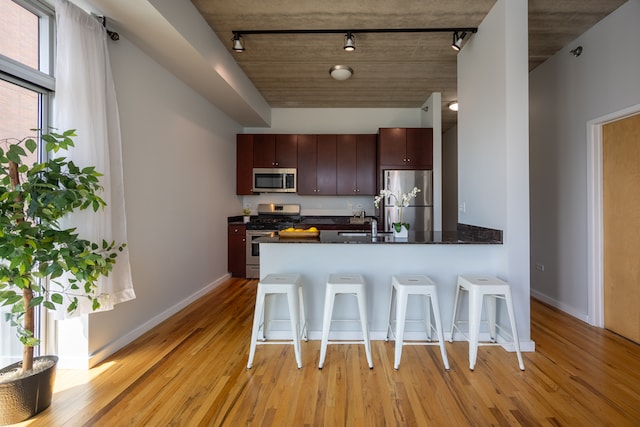 kitchen featuring appliances with stainless steel finishes, a breakfast bar area, light wood-type flooring, track lighting, and kitchen peninsula