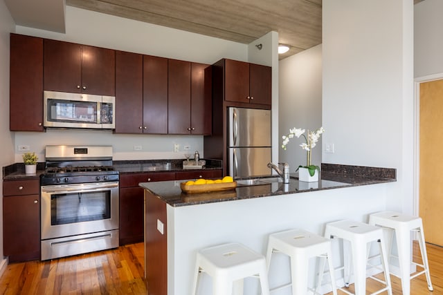 kitchen featuring hardwood / wood-style floors, appliances with stainless steel finishes, dark stone counters, kitchen peninsula, and a kitchen breakfast bar