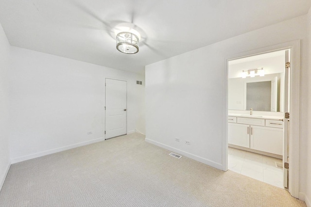 unfurnished bedroom featuring ensuite bathroom, sink, and light colored carpet