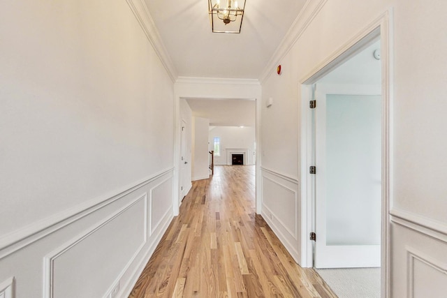 corridor with a notable chandelier, ornamental molding, and light hardwood / wood-style floors