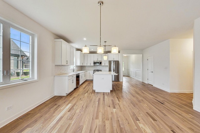 kitchen with hanging light fixtures, appliances with stainless steel finishes, a kitchen island, tasteful backsplash, and light hardwood / wood-style floors