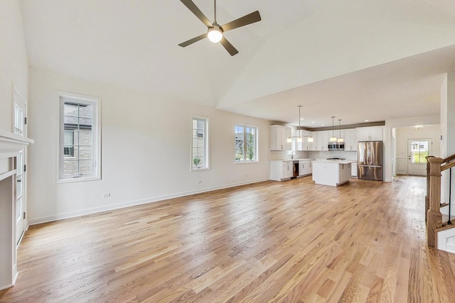 unfurnished living room featuring high vaulted ceiling, light wood-type flooring, sink, and ceiling fan