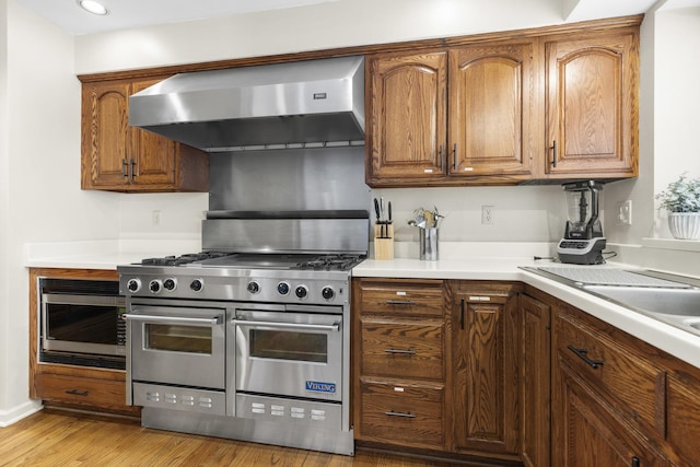 kitchen featuring built in microwave, light hardwood / wood-style flooring, exhaust hood, and range with two ovens