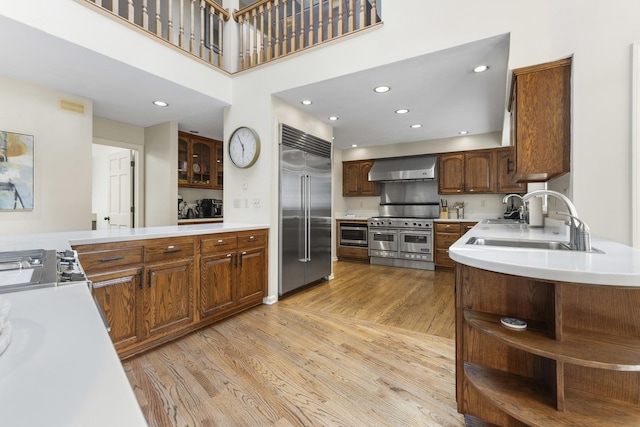 kitchen with sink, built in appliances, light hardwood / wood-style floors, kitchen peninsula, and wall chimney exhaust hood