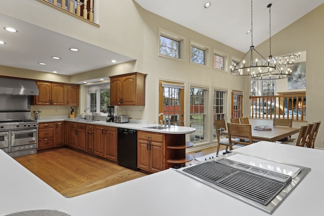 kitchen featuring decorative light fixtures, sink, black dishwasher, range with two ovens, and wall chimney range hood