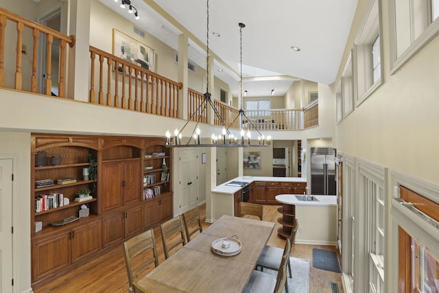 dining area with a notable chandelier, sink, a high ceiling, and light wood-type flooring