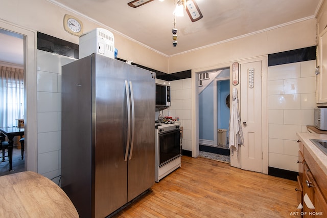 kitchen featuring light wood-type flooring, appliances with stainless steel finishes, ornamental molding, and ceiling fan