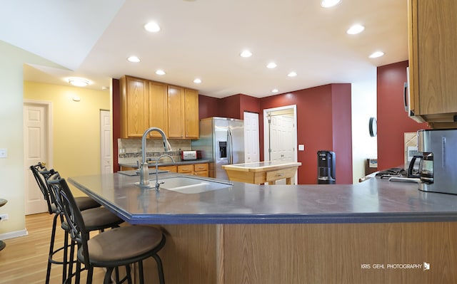 kitchen with stainless steel fridge, backsplash, kitchen peninsula, light wood-type flooring, and sink