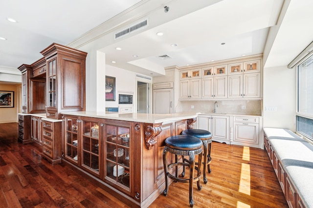 kitchen featuring crown molding, backsplash, a kitchen breakfast bar, wood-type flooring, and sink