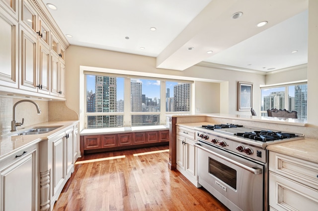 kitchen with cream cabinets, crown molding, light hardwood / wood-style flooring, sink, and luxury range