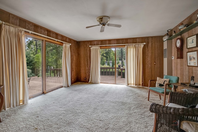 living area featuring ceiling fan, wooden walls, and carpet