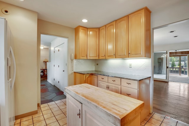 kitchen featuring light brown cabinetry, white refrigerator with ice dispenser, light tile patterned floors, and tasteful backsplash