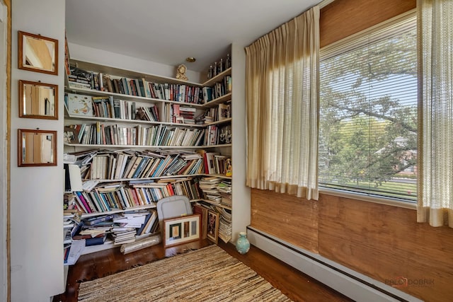 living area with a baseboard heating unit, wood-type flooring, and plenty of natural light