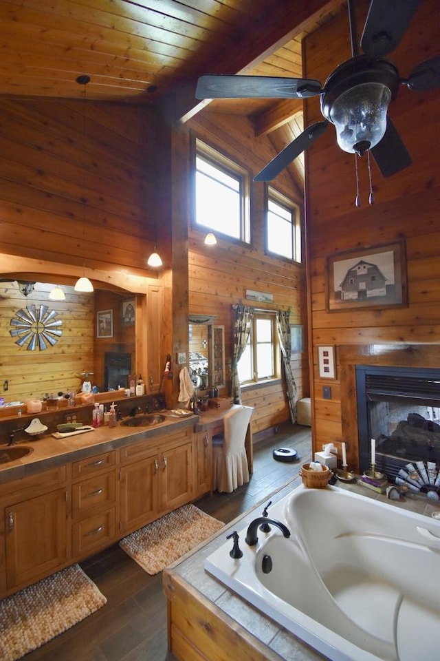 full bathroom with wooden walls, a multi sided fireplace, hardwood / wood-style floors, high vaulted ceiling, and a sink
