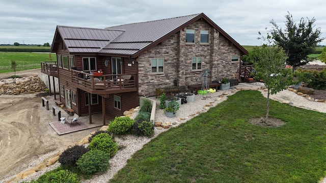 rear view of house with a deck, a standing seam roof, stone siding, and a lawn