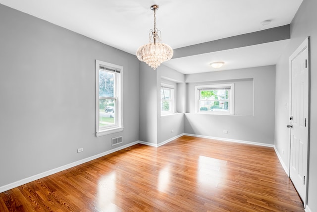 spare room featuring a notable chandelier, plenty of natural light, and wood-type flooring