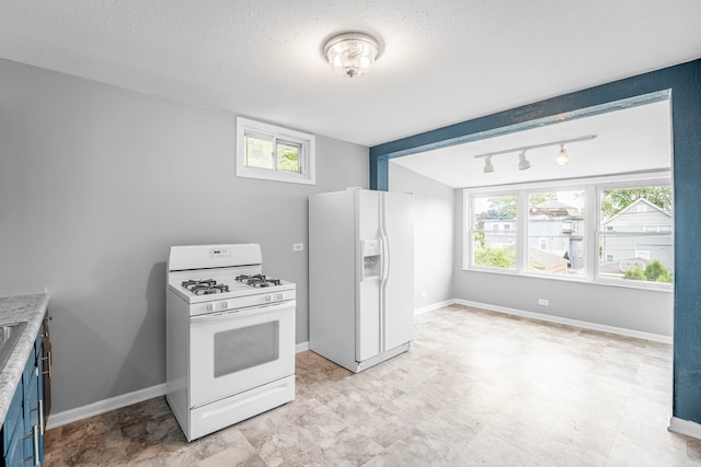 kitchen with a textured ceiling, blue cabinetry, light tile patterned flooring, white appliances, and track lighting