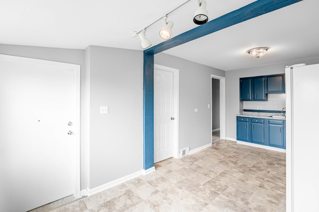 kitchen with blue cabinetry, tasteful backsplash, white refrigerator, light tile patterned flooring, and track lighting