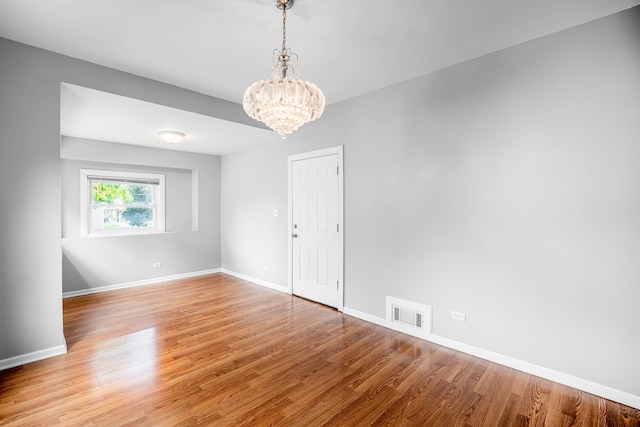 empty room with a notable chandelier and hardwood / wood-style flooring