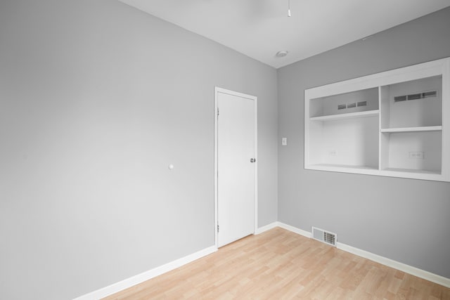 empty room featuring built in shelves and hardwood / wood-style floors