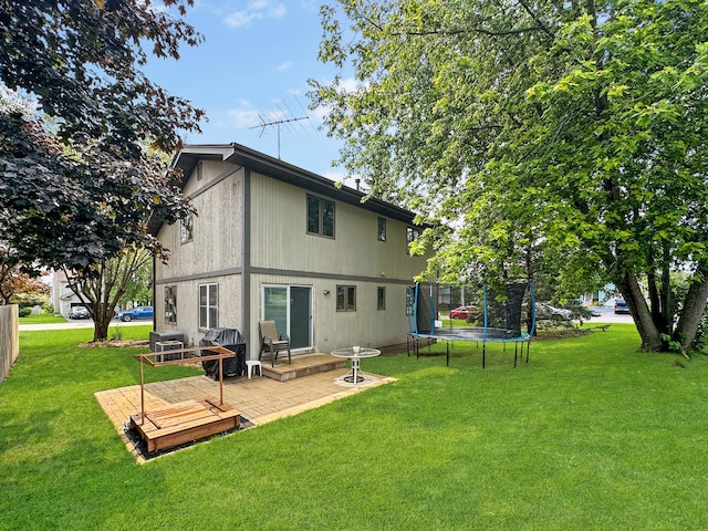 rear view of property featuring a patio, a trampoline, and a lawn