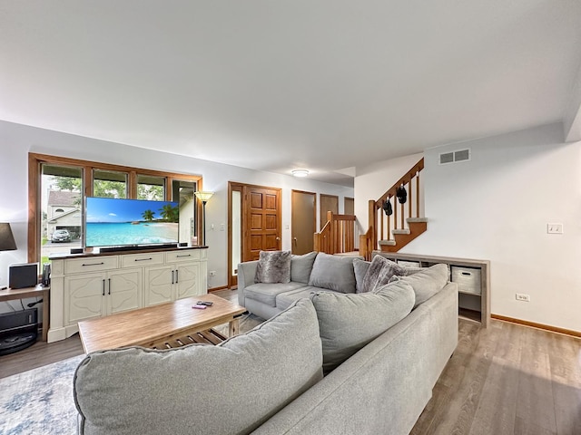 living area with stairway, wood finished floors, visible vents, and baseboards