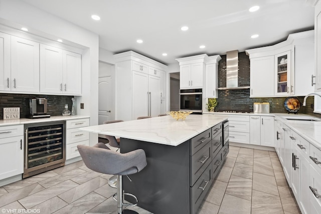 kitchen featuring a breakfast bar, sink, wall chimney range hood, beverage cooler, and white cabinets