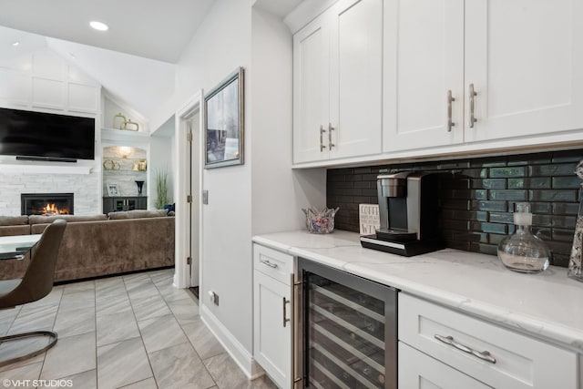 kitchen featuring a fireplace, white cabinetry, beverage cooler, decorative backsplash, and light stone counters