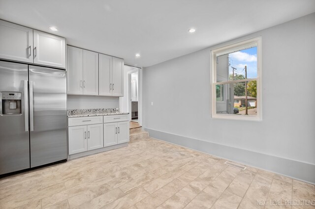 kitchen with stainless steel fridge with ice dispenser, light stone countertops, and white cabinets