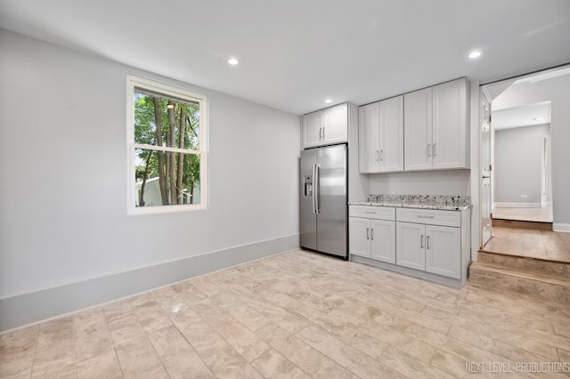 kitchen featuring light stone countertops, white cabinetry, light tile patterned floors, and stainless steel refrigerator with ice dispenser