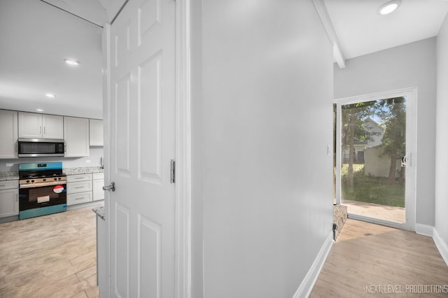 hallway featuring light wood-style flooring, baseboards, and recessed lighting