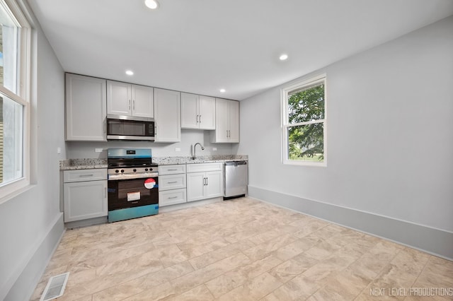 kitchen with sink, stainless steel appliances, light tile patterned floors, and light stone counters