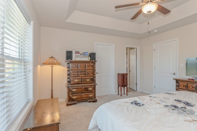 bedroom featuring light carpet, multiple windows, ceiling fan, and a raised ceiling