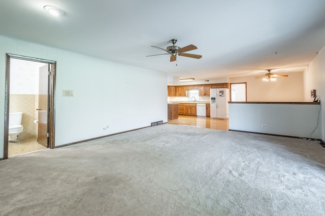 unfurnished living room featuring ceiling fan, light colored carpet, and sink