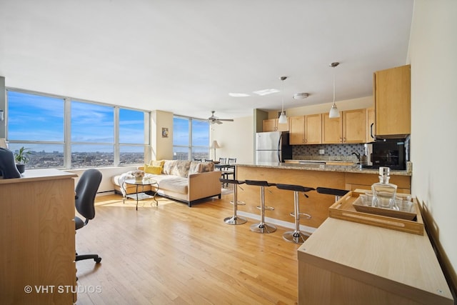 kitchen featuring a peninsula, a kitchen bar, light brown cabinets, light wood-style floors, and freestanding refrigerator