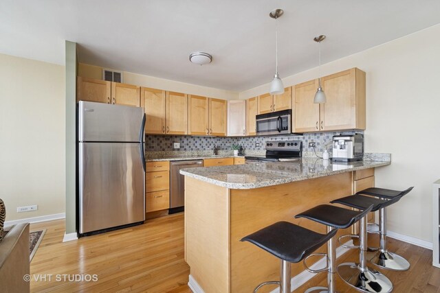 kitchen with backsplash, appliances with stainless steel finishes, a peninsula, light wood-style flooring, and visible vents