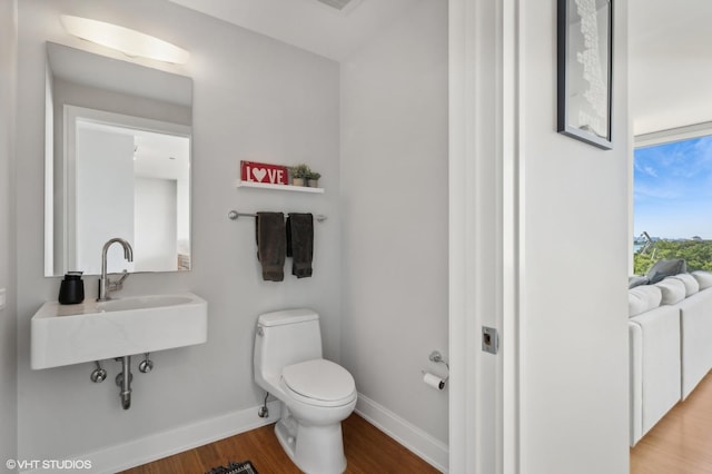 half bath featuring a sink, wood finished floors, toilet, and baseboards