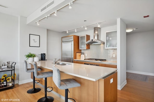 kitchen with a sink, visible vents, light wood-style floors, wall chimney range hood, and decorative backsplash