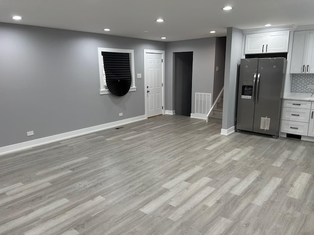 kitchen with decorative backsplash, white cabinets, light hardwood / wood-style floors, and stainless steel fridge with ice dispenser