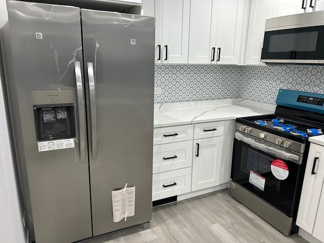 kitchen with appliances with stainless steel finishes, light stone counters, light hardwood / wood-style floors, tasteful backsplash, and white cabinets