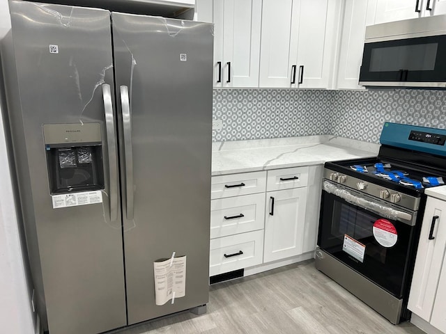 kitchen featuring appliances with stainless steel finishes, tasteful backsplash, white cabinets, light stone counters, and light hardwood / wood-style flooring