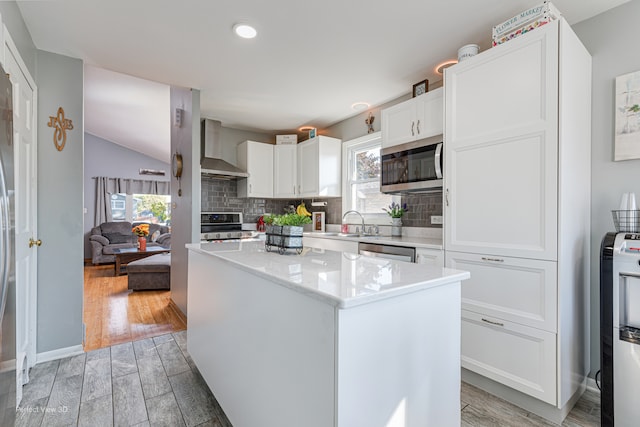 kitchen with appliances with stainless steel finishes, a healthy amount of sunlight, a kitchen island, and wall chimney range hood