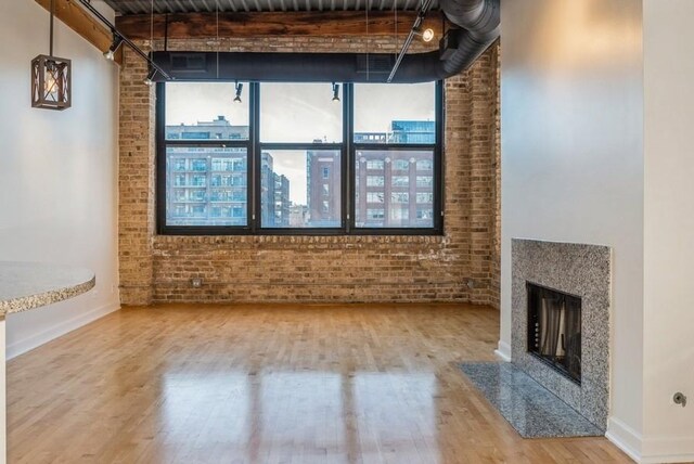 unfurnished living room featuring beamed ceiling, brick wall, a premium fireplace, and wood-type flooring